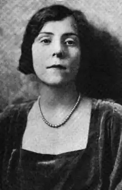 A young white woman with dark hair, wearing a velvet dress with a square neckline, and a strand of pearls or beads