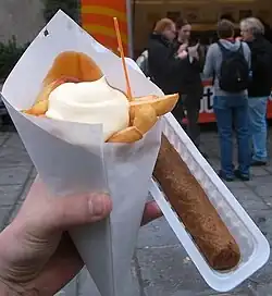 Image 125Frites wrapped in a traditional paper cone (cornet) served with mayonnaise and curry ketchup, with a small plastic fork on top and a meat frikandel on the side (from Belgian cuisine)