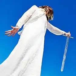 A woman in white robes holding a sword against a backdrop of the sky