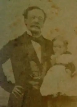 Brown facing forwards, with his daughter on his hip