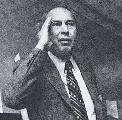 Lois holding his hand to his head, wearing a suit in a black-and-white photograph