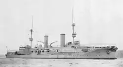 A large, light gray ship with two tall masts and two smoke stacks