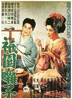 A painting of two women wearing kimono kneeling down on a floor. The woman on the left wears a blue kimono, the woman on the right a pink kimono with a traditional hairstyle. Japanese text is written in the top left, bottom right, right-hand side and left-hand side of the image.