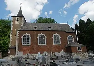 Religious building in brick in Neo-Romanesque style. In the foreground, a cemetery, in the background, a forest.