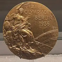 A tarnished gold medal featuring a person in a toga, and the words "XI Olympiade Berlin 1936".