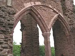 Part of a castle, with a huge semi-circular arch containing two smaller Norman arches dominating the picture. Through the arches, a ruined pillar can just be made out.