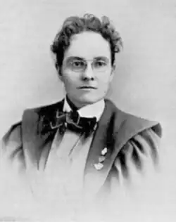 19th-century B&W portrait photo of a woman wearing a white blouse, dark bow tie, and dark jacket, with her hair in an up-do.