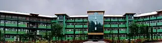 View of the main building of Green Valley Educational Institute in Srinagar, taken from the south side, showing its green and cream-colored façade, large windows, central entrance, and surrounding landscaped grounds.