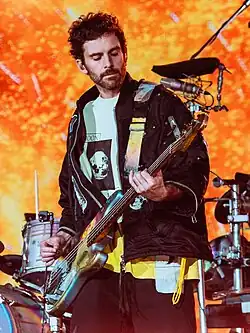Berryman on stage with his bass, wearing a yellow shirt and a black jacket