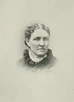 B&W portrait photo of a middle-aged woman wearing a dark, high-collared blouse with her hair in an up-do.