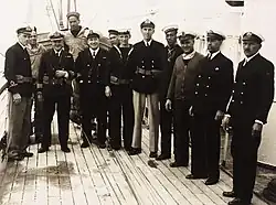 Crew, including two Government Pilots at right, of Royal Naval Examination Service vessel HMS Castle Harbour at the British Imperial fortress colony of Bermuda during the Second World War. The vessel delivered a naval examiner and pilot to arriving ships, respectively to clear them for entry and to steer to harbour.