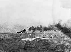 A large ship is sinking in the distance; a large dense cloud of smoke emanates from the wreck.