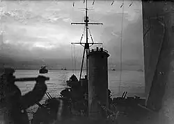 View from the cruiser HMS&nbsp;Sheffield as she sails on convoy duty through the waters of the Arctic Ocean. In the background are merchant ships of the convoy. The image was taken during the twilight of the arctic winter—the short time each day that the sun is seen during winter near the pole. In the foreground is the silhouette of a lookout using a telescope.