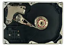 An HDD with disks and motor hub removed, exposing copper-colored stator coils surrounding a bearing in the center of the spindle motor. The orange stripe along the side of the arm is a thin printed-circuit cable, the spindle bearing is in the center and the actuator is in the upper left.