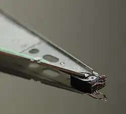 Close-up of an HDD head resting on a disk platter; its mirror reflection is visible on the platter surface. Unless the head is on a landing zone, the heads touching the platters while in operation can be catastrophic.