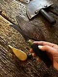 A hand holds the handle of the Harness maker's knife, which has a short, curved blade.