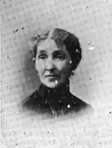 B&W portrait photo of a middle-aged woman wearing a dark, high-collared blouse with her hair in an up-do.