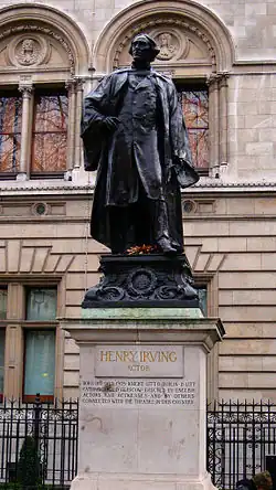 Bronze statue of clean-shaven white man in modern (c. 1900) clothes and academic gown, holding a manuscript, atop approximately 12-foot-high marble pedestal engraved with the caption "Henry Irving: Actor" and some facts about Irving and an the people who erected the statue