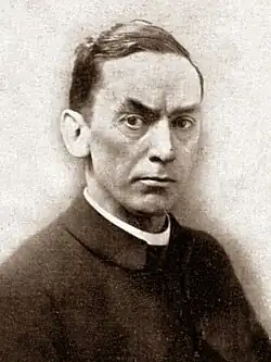Black and white photograph of clean-shaven white man of middle age, with short dark hair, wearing clerical dress