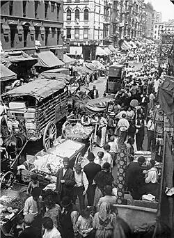 A wide street, packed with people and wagons