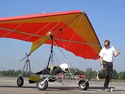 The kite hang glider is readying for being a kite in two ways; during kiting tug by the ultralight powered hang glider trike the system is a long-line kite being towed; then upon release from tug, the kite hang glider is a short-kite-lined free-flight kite with a dominant aim of gliding.