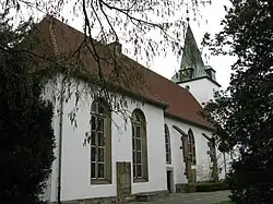 A stone church with a tall, dark steeple under a partly cloudy sky.