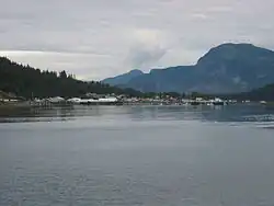 Coastal view of Hoonah, Alaska, showing waterfront buildings backed by forested hills and mountains along an inlet in southeastern Alaska.