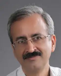 A portrait photograph of Hooshmand Dehghan, an Iranian scholar and translator with glasses.