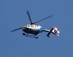 A blue and white painted helicopter flying in blue sky, pictured from below.
