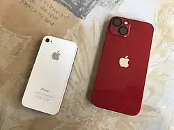 Back view of a (PRODUCT)RED iPhone 13 alongside a white iPhone 4s. Note the camera protector installed on the iPhone 13.