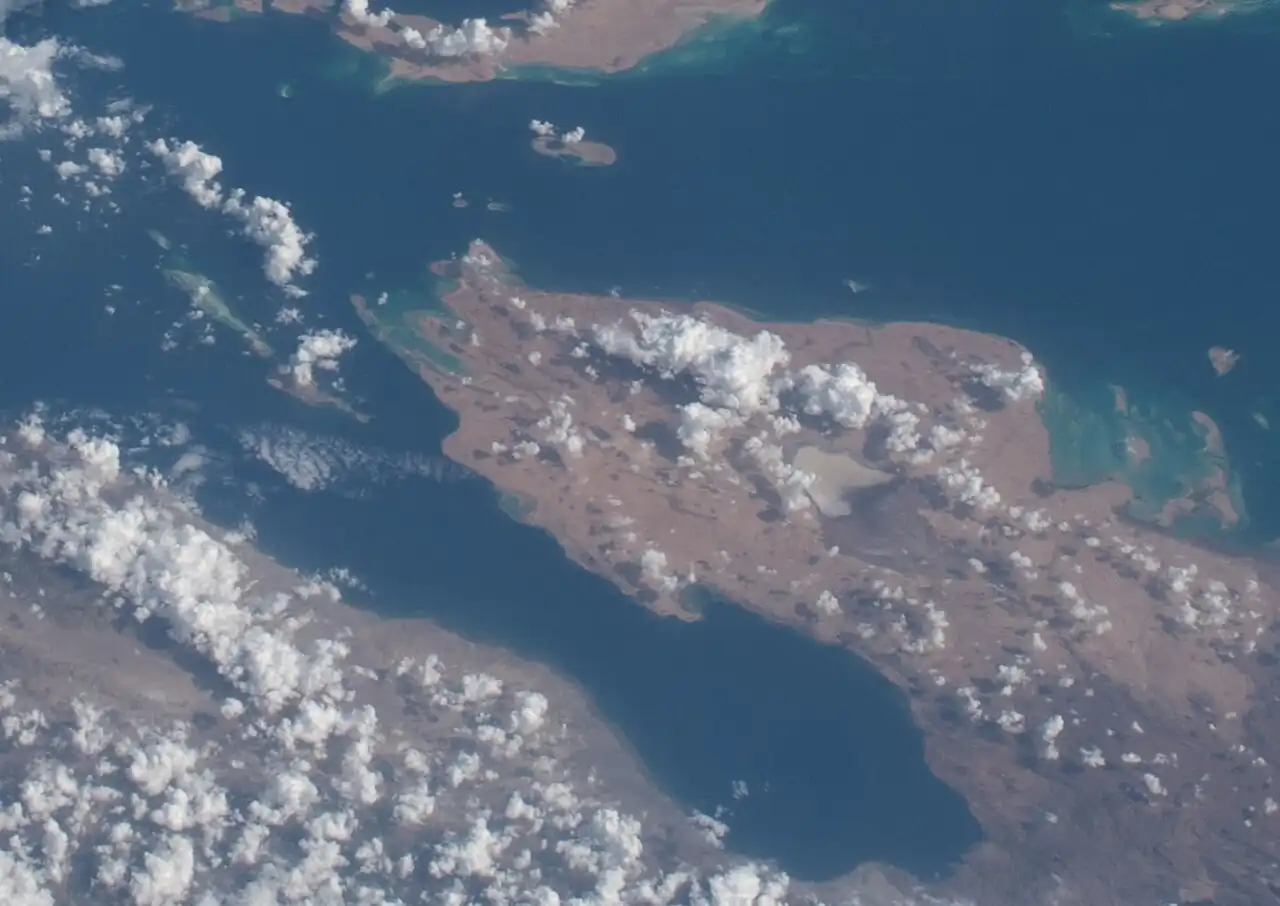 Buri Peninsula in the middle, clouds and a grey lake, island Shumma and dark blue Massawa Channel of Red Sea in upper part, some coastal islands in the right side in light blue water, Dessie and long coral reef in left side, Gulf of Zula - a long bay