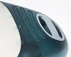 Detail of the back of a curved, blue-green translucent computer; a white plastic handle and ventilation hole are visible.