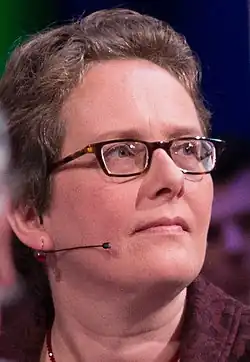 close-up of Ingrid Robeyns from profile, wearing a microphone headset, looking left and slightly up with set face