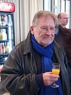 A smiling person wearing a leather jacket and holding a glass
