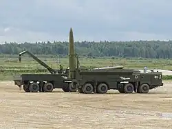 A 9P78-1 launcher in foreground and a 9T250 transloader in the background