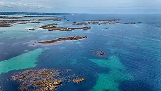 Aerial photograph showing shallow turquoise water and scattered rocky outcrops forming tidal flats near Roscoff in Brittany, France.
