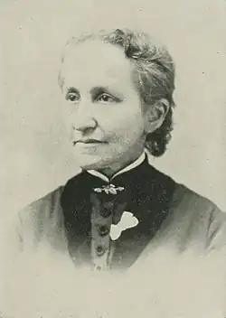 19th-century B&W portrait photo of a woman with her hair in an up-do, wearing a dark, fitted blouse.