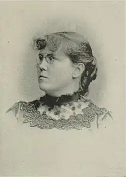 19th-century B&W portrait photo of a woman with her hair in an up-do, wearing a dark, fitted blouse.