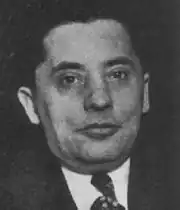 Black-and-white mugshot of Zuta in a suit