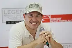 A smiling man in a short-sleeved shirt holding a microphone.