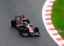 A navy blue and red Formula One car being driven at speed on a dry circuit