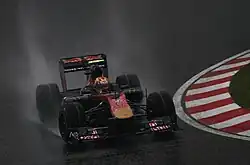 A navy-and-gold single-seater racing car is driven around a drenched tarmac course.