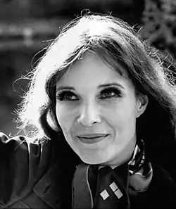 A black-and-white portrait of a woman with long hair and expressive eyes smiles softly while looking upward
