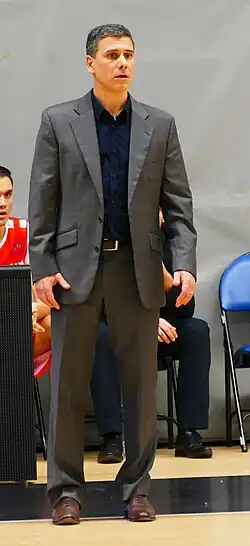 A tall man in a gray suit looks at the foreground, concentrating
