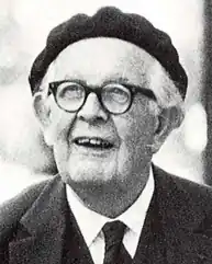 Photo of a man with white hair and glasses, wearing a suit