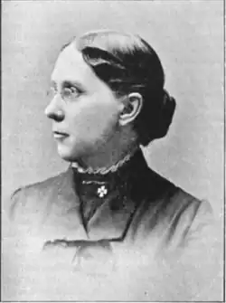 19th-century B&W portrait photo of a woman with her hair in an up-do, wearing a dark, fitted blouse.