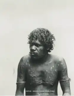 Portrait photograph of a shirtless Aboriginal man with a scarred torso