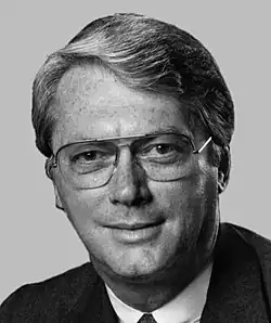 A color portrait of a gray-haired man in his seventies wearing a suit