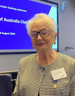 Dr Joan Benjamin stands in front of a screen welcoming recipients of Australian Honours at a ceremony held in Geelong on 29 August 2024