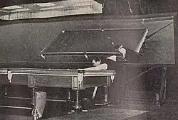 Joe Davis playing at a billiard table, with a large mirror behind him reflecting the table